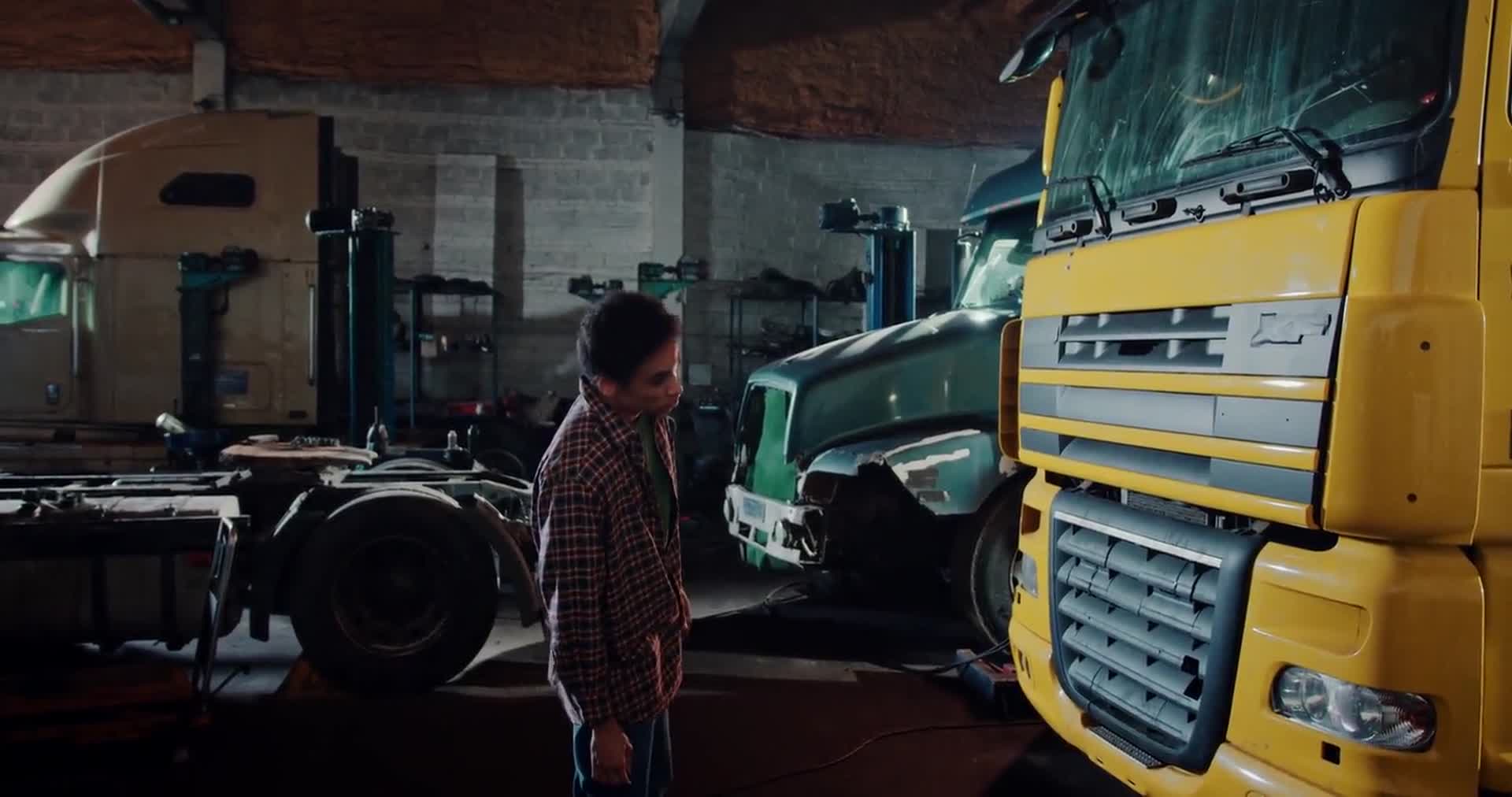 Heavy trucks in a workshop bay, a mechanic walking between them