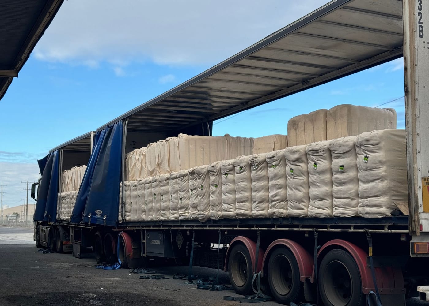 A curtainsider trailer with its curtains open, loaded with wool bales